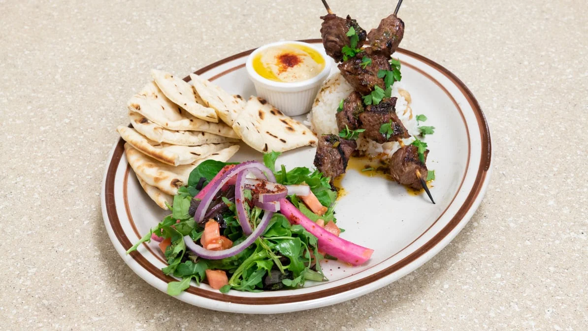 Lamb Shish Kebab - Tender marinated lamb skewers grilled over an open flame, served with chimichurri sauce and fresh sides.