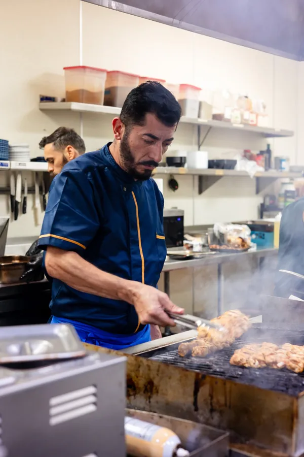 Kalimera chef turning chicken skewers on the grill with tongs