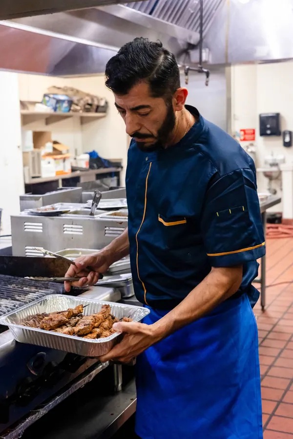 Kalimera chef carrying a tray of grilled meat skewers from the grill
