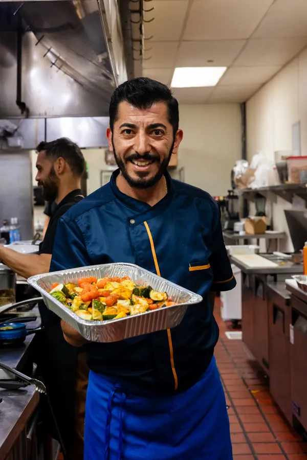 Kalimera chef holding a tray of roasted vegetables in the kitchen