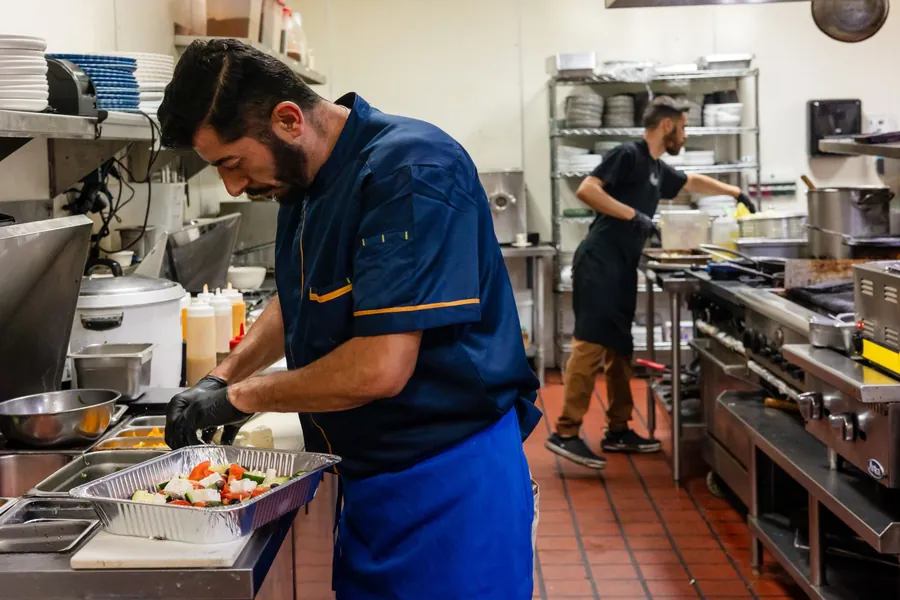 Kalimera chef assembling a Greek salad tray with feta, tomato, cucumber and olives
