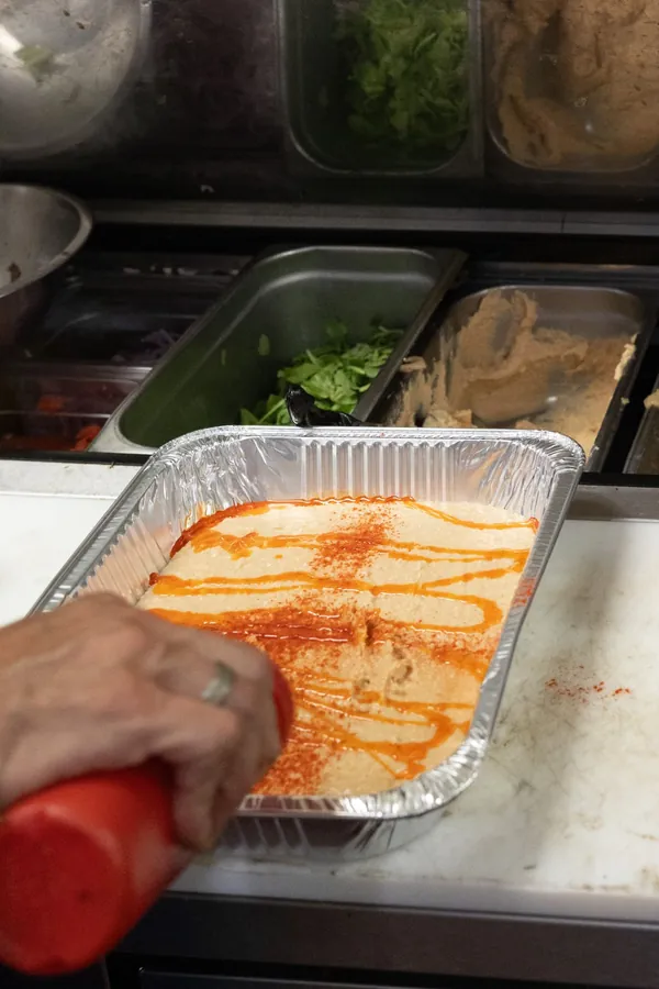 Hummus tray being finished with a drizzle of sauce and paprika