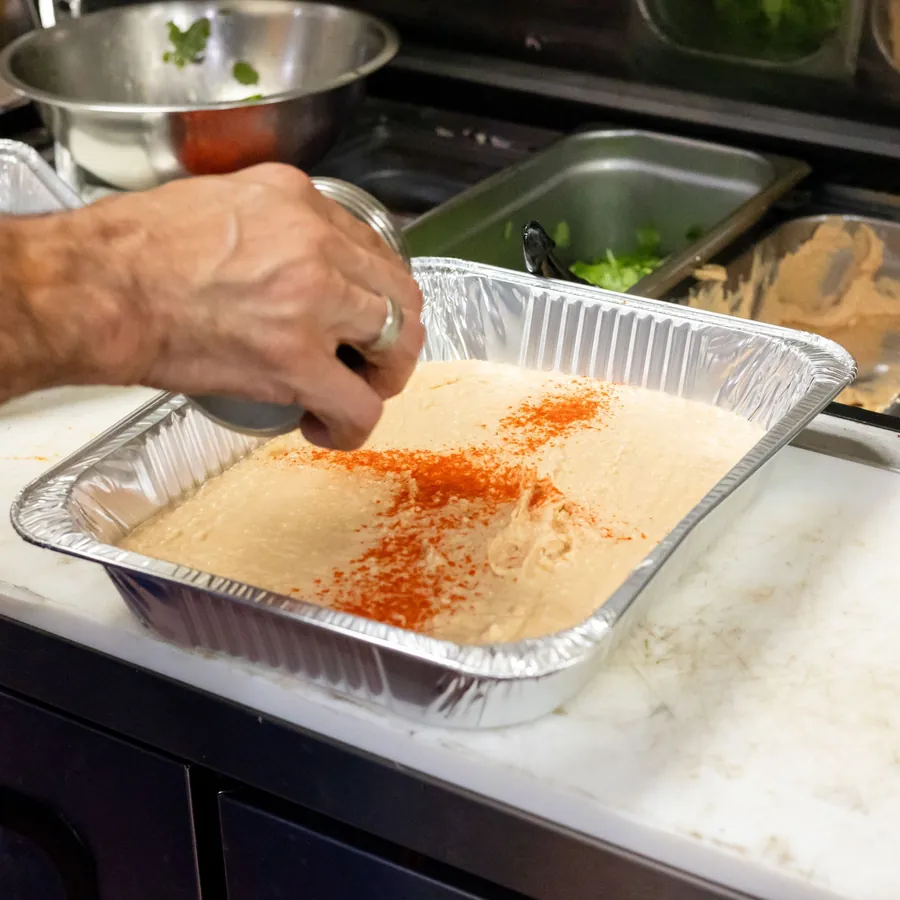 Hand dusting a tray of hummus with paprika