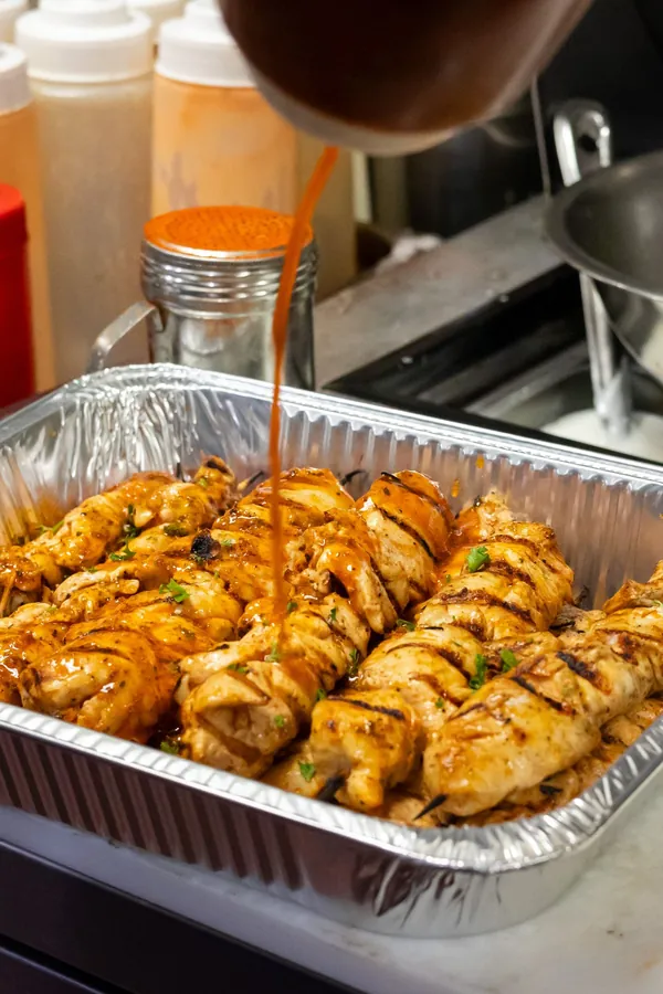 Sauce poured over a tray of grilled chicken skewers