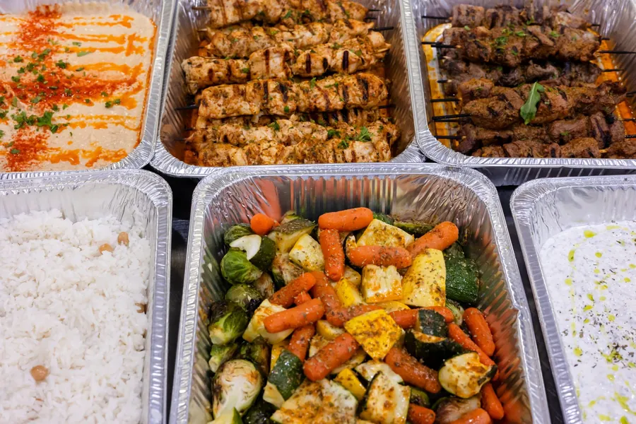Six catering trays of hummus, skewers, chickpea rice, roasted vegetables and tzatziki