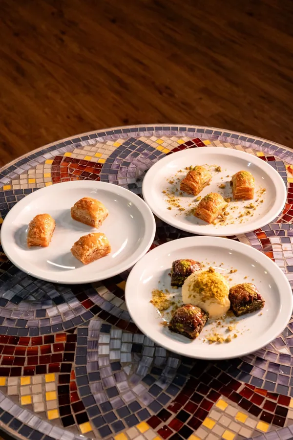 Three plates of baklava pieces on a mosaic table, one served with ice cream