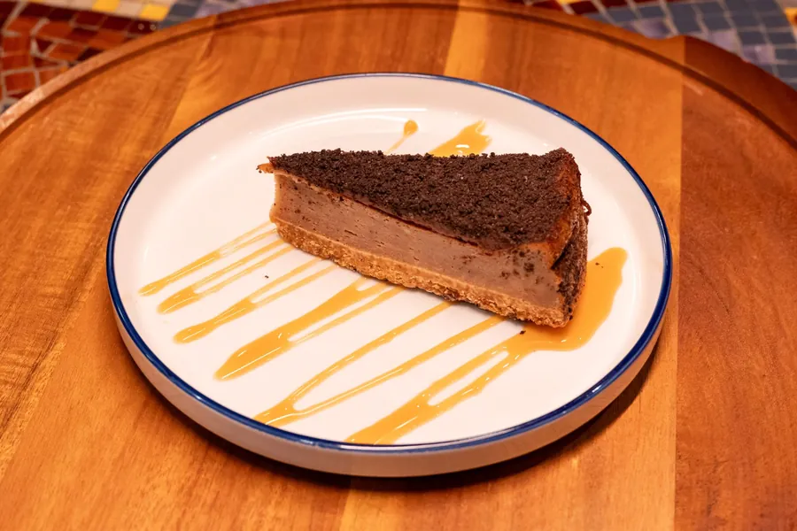 Slice of baked cheesecake with a cookie crumb top and caramel drizzle