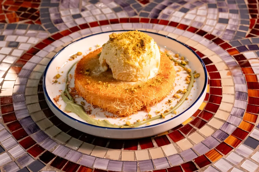 Golden shredded-pastry dessert topped with a scoop of ice cream and crushed pistachio