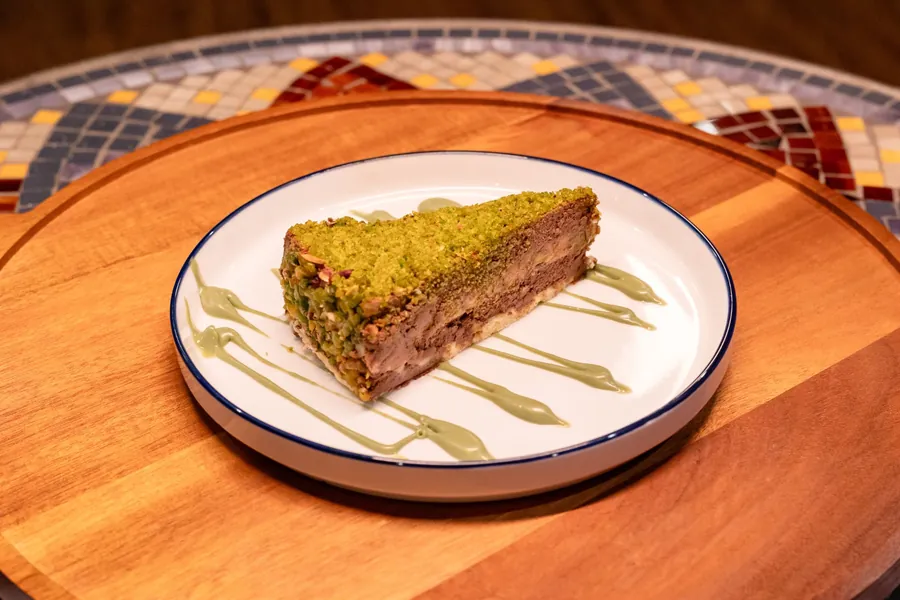 Slice of cake with a pistachio top, a chocolate cream layer and pistachio sauce