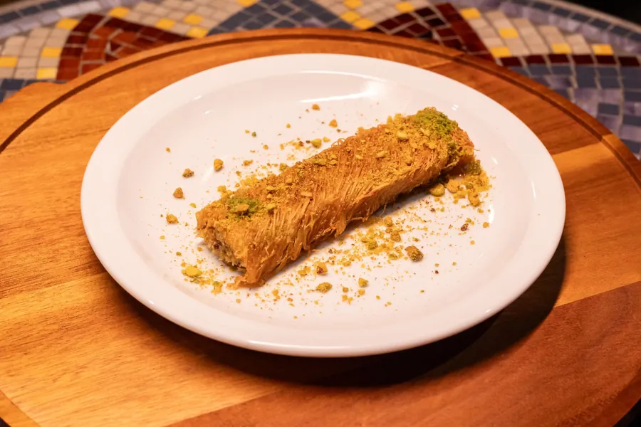 Rolled shredded-pastry dessert sprinkled with crushed pistachio