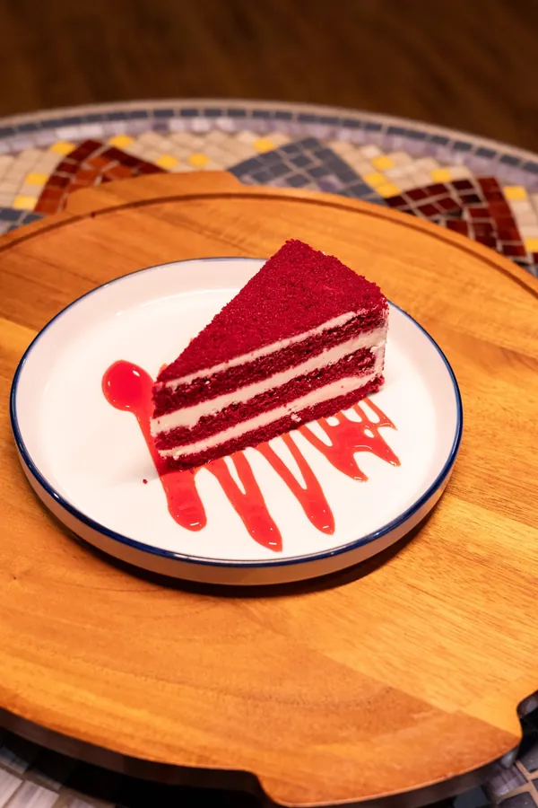 Slice of red velvet cake with cream layers and a red berry sauce