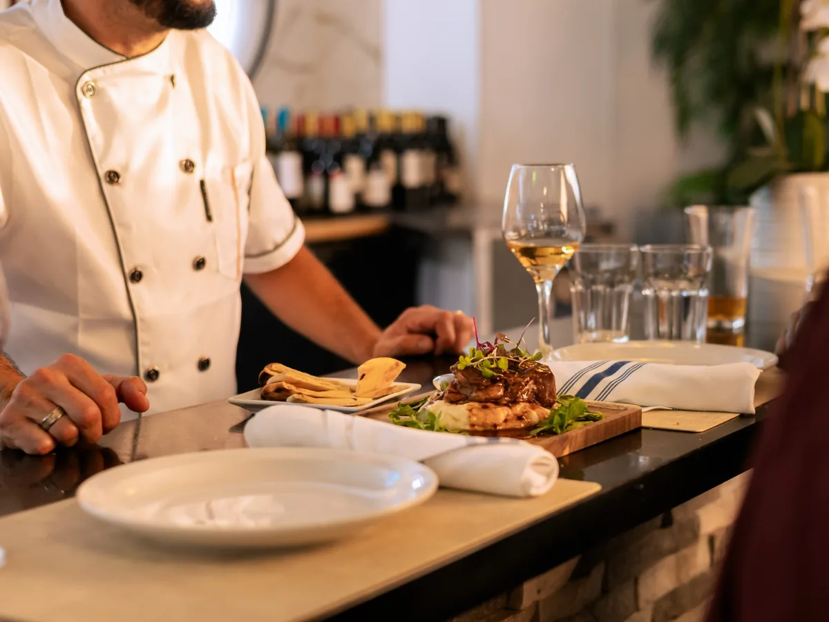 Chef plating a signature dinner dish at the Kalimera bar with wine